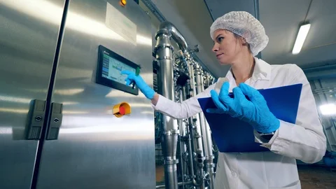 Plant worker checks a machine, typing on display. Female worker controls the Stock Footage 121250698