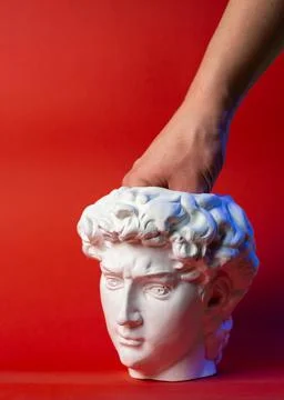 Plaster pot in the form of David's head and male hand on a red background. Stock Photos
