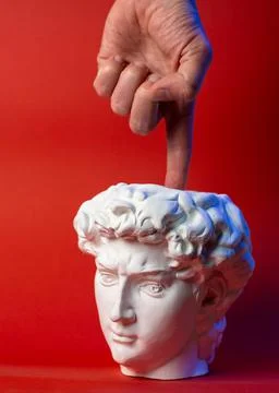 Plaster pot in the form of David's head and male hand on a red background. Stock Photos