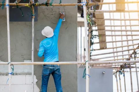 Plasterer in blue working uniform plastering the wall of house building site. Stock Photos