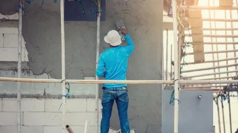 Plasterer in blue working uniform plastering the wall of house building site. Stock-Fotos