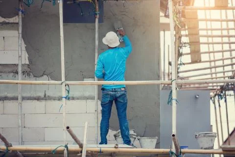 Plasterer in blue working uniform plastering the wall of house building site. Stock Photos