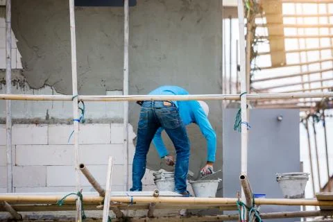 Plasterer in blue working uniform plastering the wall of house building site. Stock Photos