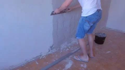 Plasterer man is aligning wet plaster on wall using long metal tool spatula. Stock Footage 153413044
