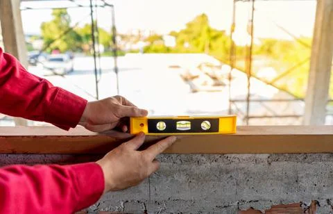 Plasterer in red working uniform check balance of wood window frame, check ce 스톡 사진