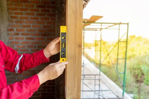 Plasterer in red working uniform check balance of wood window frame, check ce Stock Photos