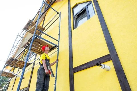 Plasterer on scaffolding working on facade, applying plaster, leveling wall.. Stock Photos