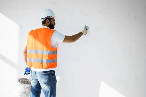 Plasterer in workwear smoothing wall surface of building indoors Fotos de archivo