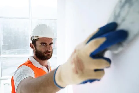 Plasterer in workwear smoothing wall surface of building indoors Fotos de archivo