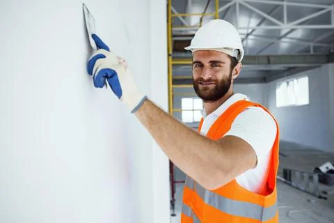 Plasterer in workwear smoothing wall surface of building indoors Fotos de archivo