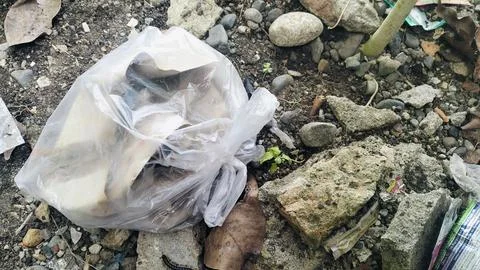 Plastic bag filled with garbage abandoned on dirty soil ground. Stock Photos