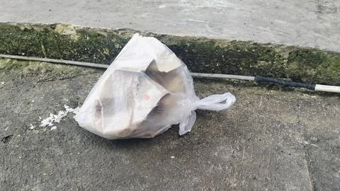 Plastic bag filled with garbage abandoned on dirty soil ground. Stock Photos