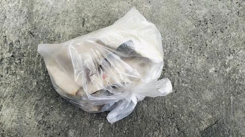 Plastic bag filled with garbage abandoned on dirty soil ground. Stock Photos