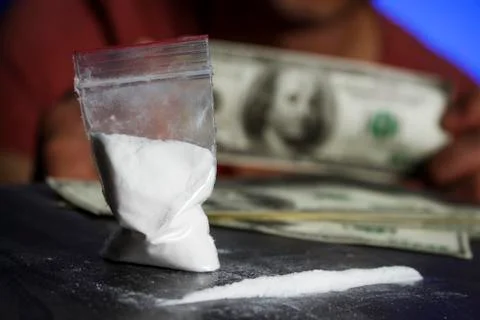 Plastic bag with white powder on the background of a young guy with dollars Stock Photos