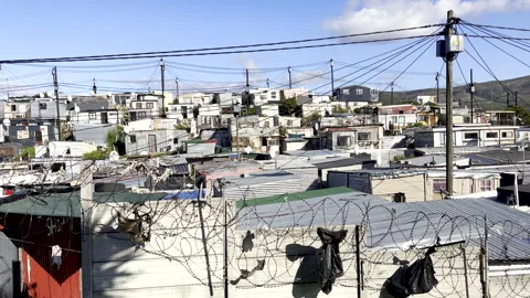 Plastic bags stuck on coiled razor wire next to sprawling township tin shacks Stock Footage 331280423