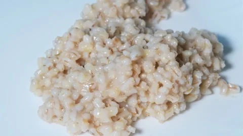 Plastic black spoon puts boiled pearl porridge in white plate from which hot ste Stock Footage 247018530