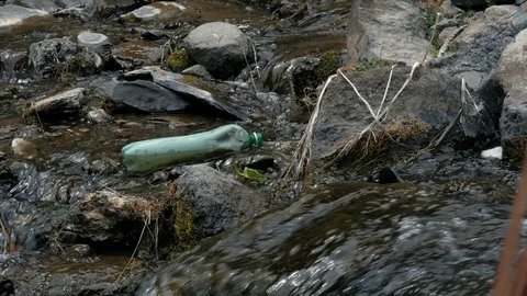 Plastic bottle and pollution in mountain river washes up onto stones Stock Footage 90347928