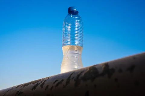 Plastic bottle balanced on rocky edge against clear blue sky outdoor minimalist Stock Photos