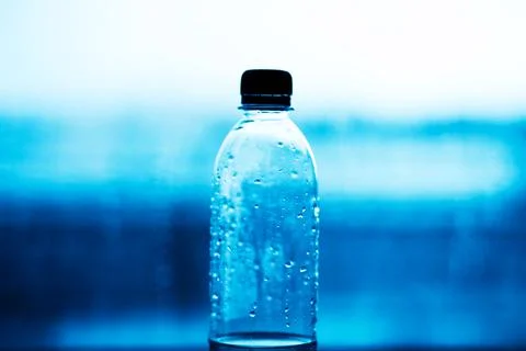 A plastic bottle with a black lid half filled with clean water stands against Stock Photos