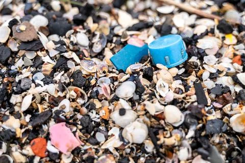 Plastic bottle cap among seashells and pebbles Stock Photos