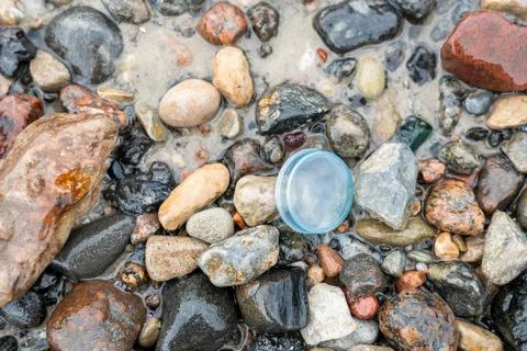 Plastic bottle cap on pebble beach, close-up, ocean plastic pollution Stock Photos