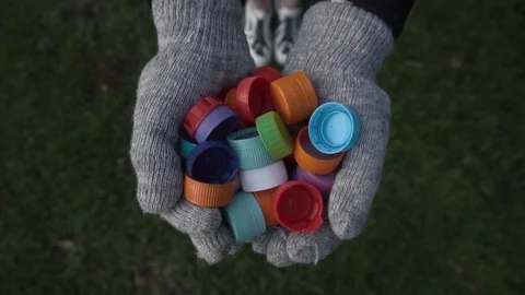 Plastic bottle caps fall on the lawn from the hands of a girl in gloves Vidéo 120089986