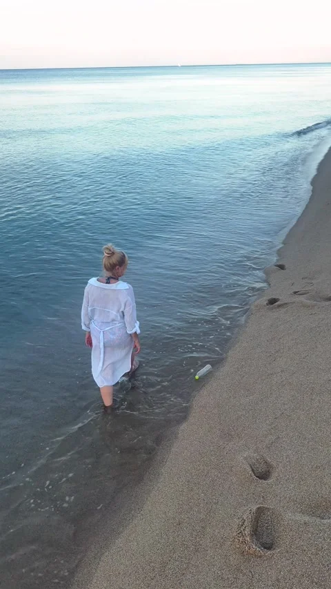 Plastic bottle left on the beach drifts into the sea as a woman walks away Stock Footage 338074568