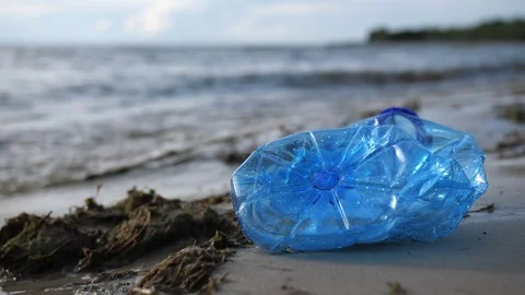 A plastic bottle lies on the seashore. The waves hit the shore. Polluted beach Stock Footage 117844858