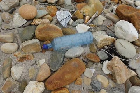 Plastic bottle polluting a pebble beach: environmental damage Stock Photos