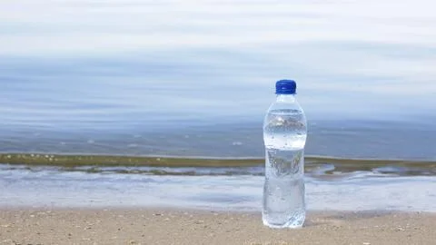 Plastic bottle with refreshing drink on sandy beach near sea, space for text. Stock-Fotos