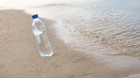 Plastic bottle with refreshing drink on sandy beach near sea, space for text. Stock-Fotos