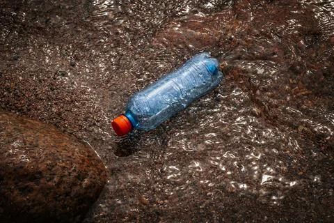 A plastic bottle by the rocks on the seashore. Garbage on the seashore Stock Photos