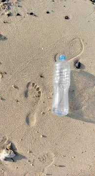 Plastic bottle in the sand, next to the footprints Stock Photos