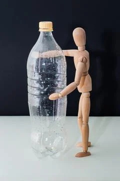 Plastic bottle without water and wooden mannequin on black background Фото