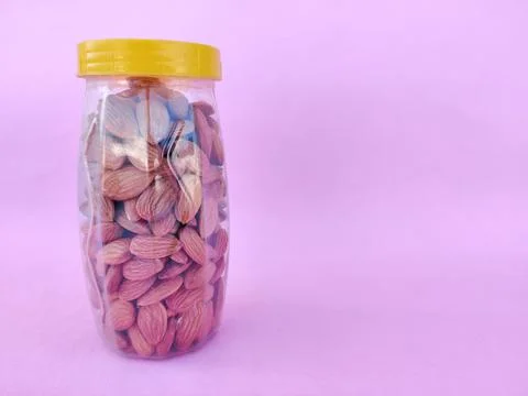 A Plastic bottle with yellow cap is filled with healthy almonds. Pink backgro Stock Photos