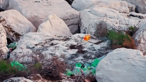 Plastic bottles and trash scattered between white rocks near the sea, showing Stock Footage 335915901