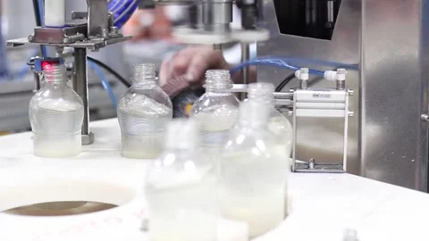 Plastic bottles are filled with clear liquid on a conveyor belt at a factory Stock Footage 134198683
