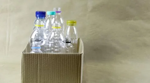 Plastic bottles in a box on a brown surface, awaiting recycling. Stock Photos