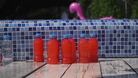 Plastic bottles with orange drink next to the swimming pool 스톡 동영상 136809975