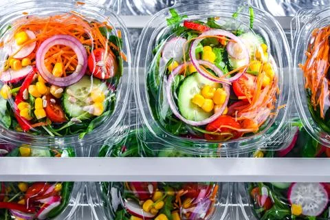 Plastic boxes with pre-packaged vegetable salads, put up for sale in a commer Stock Photos