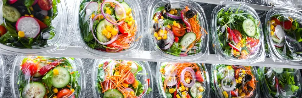 Plastic boxes with pre-packaged vegetable salads, put up for sale in a commer Stock Photos