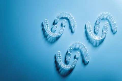 Plastic braces in the shape of a pattern lie on a blue background, dental care Stock Photos