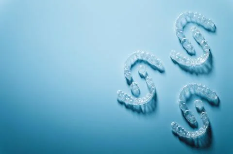 Plastic braces in the shape of a pattern lie on a blue background, dental care Stock Photos