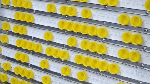 Plastic caps for PET bottles lie in rows on a packaging conveyor for further  Stock Photos