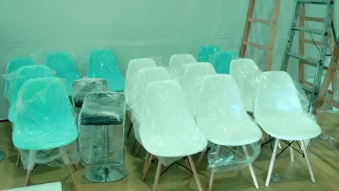 Plastic chairs covered with polyethylene stand compactly next to stepladders Stock Footage 333417495