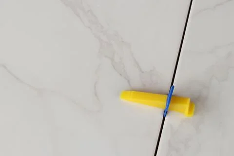 Plastic clamp and wedge at the joint of porcelain tiles with a marble pattern Stock Photos