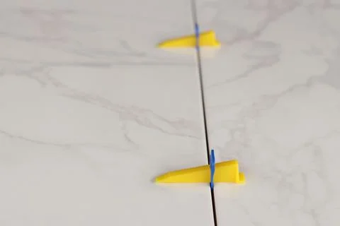 Plastic clamp and wedge at the joint of porcelain tiles with a marble pattern Stock Photos