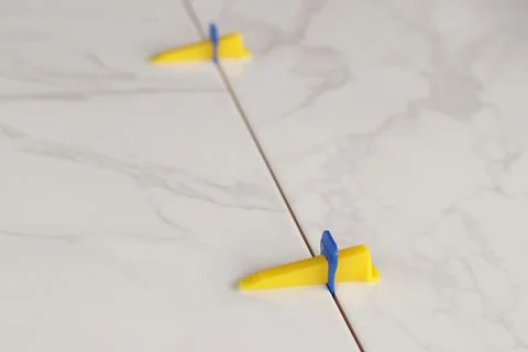 Plastic clamp and wedge at the joint of porcelain tiles with a marble pattern Stock Photos