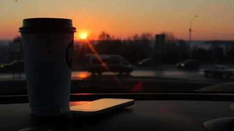 Plastic coffee cup, smartphone on car panel sunset city road traffic background Stock Footage 74999482