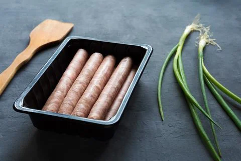 In plastic container on gray background several sausages in form of semi-finish  Stock Photos